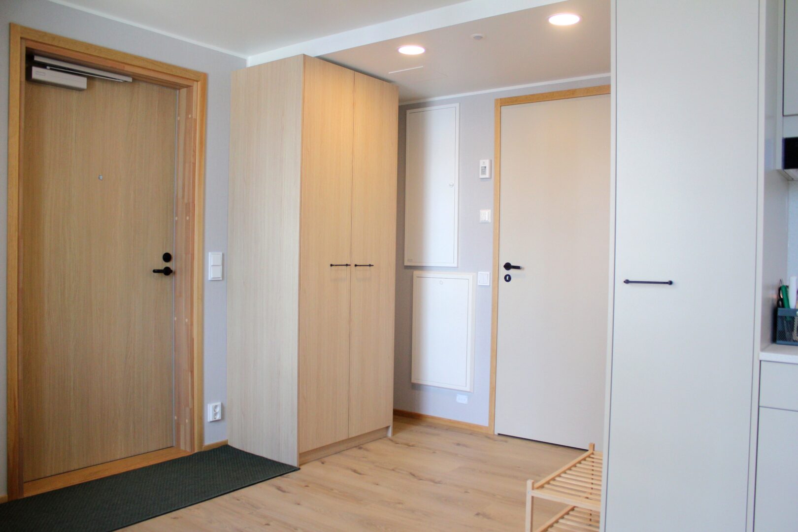 Entryway with light wood doors and tall cabinetry, gray walls, and a small bench rack along the right wall.
